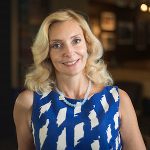 Headshot of Professor Karina Korostelina. She is smiling at the camera wearing a blue and white dress and beaded necklace.