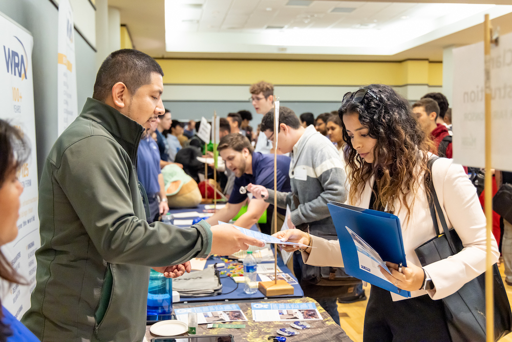 man talks to young woman at career fair table