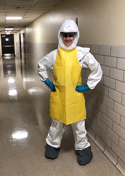 A woman smiles from under a hazmat suit helmet.