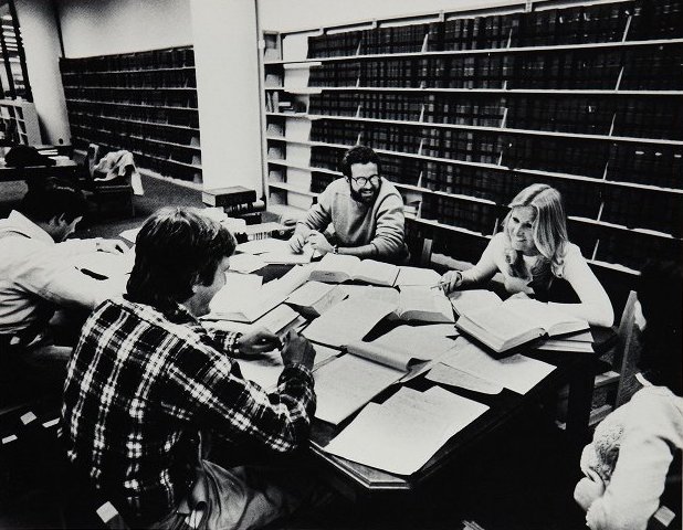 Students smile and laugh as they sit at a library table to study.