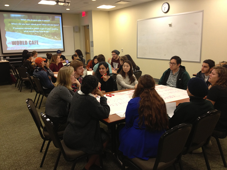 Students at three rectangular tables having discussions with one another.