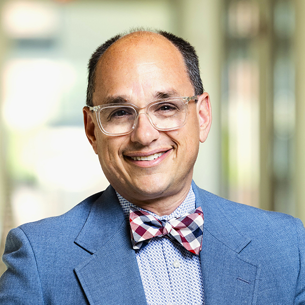 Smiling man wearing glasses and a blue suit with red, white, and blue plaid bow tie.