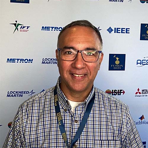 Paulo Costa wears glasses, a lanyard, and a gray shirt