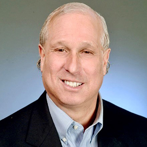 A man in a blue sport coat and a blue shirt smiles at the camera.