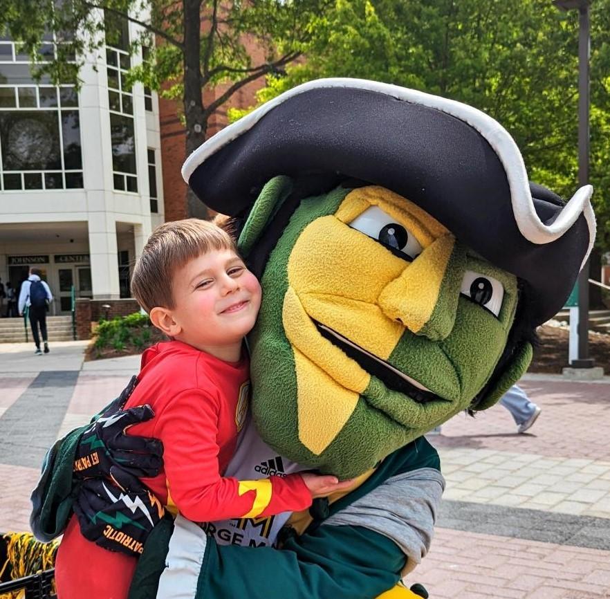 Young child hugs the Patriot mascot in front of the Johnson Center