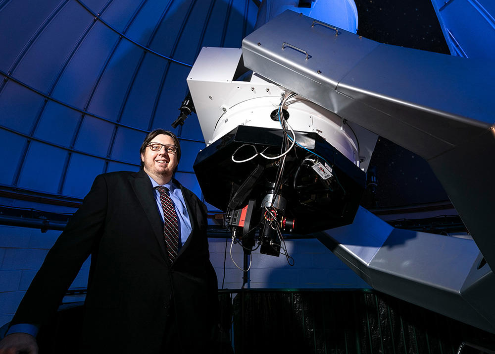 Astronomy professor Peter Plavchan stands in front of a telescope in the George Mason Observatory