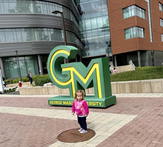 Toddler stands in front of the new George Mason logo installation on Wilkins Plaza